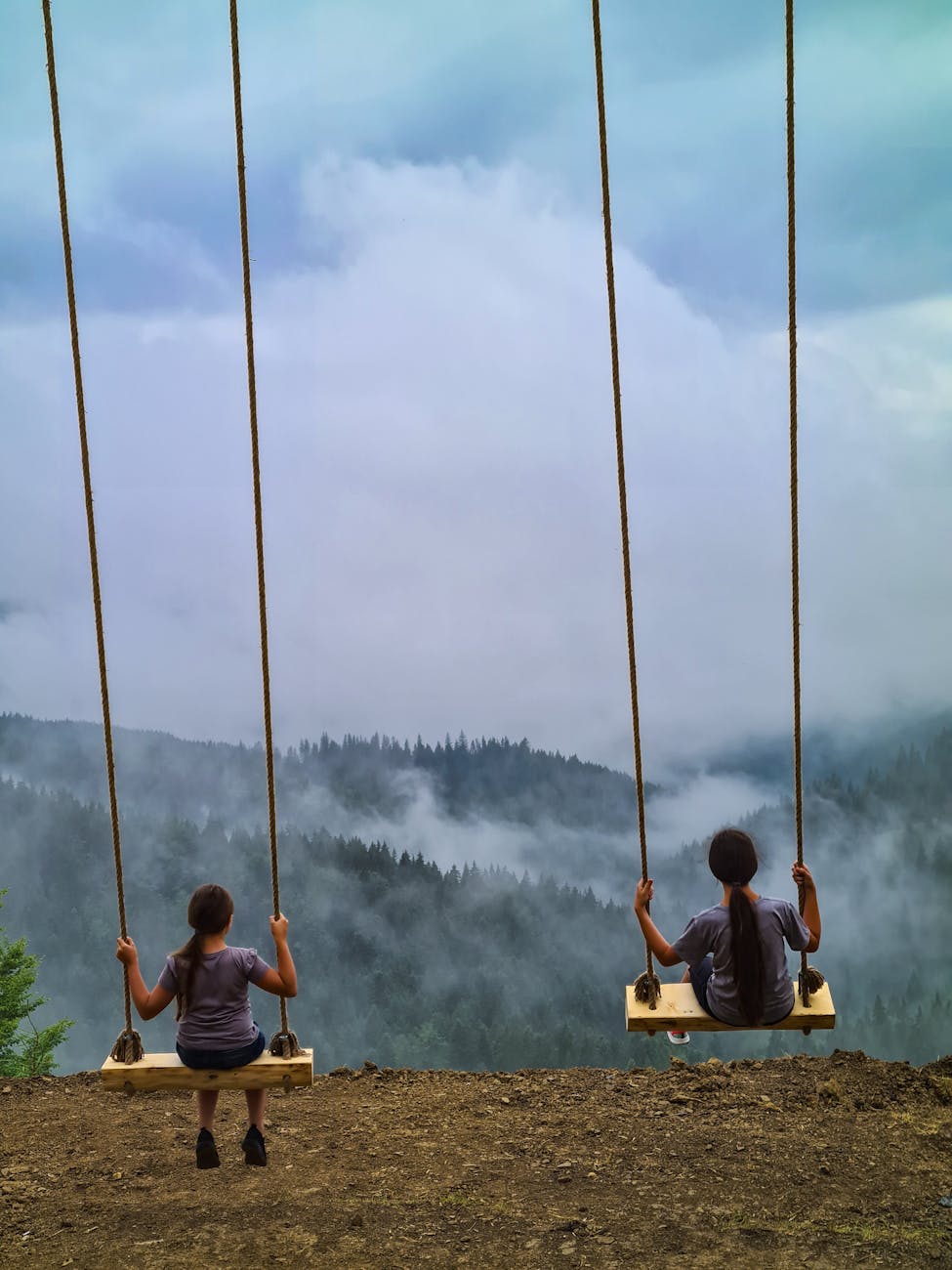 Two girls enjoying swings with a stunning view of Sucevița mountains in Romania, creating a serene family moment.